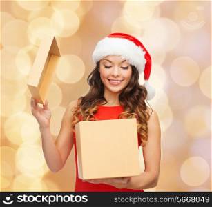 christmas, holidays, celebration and people concept - smiling woman in santa helper hat with gift box over beige lights background