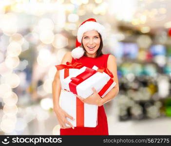 christmas, holidays, celebration and people concept - smiling woman in santa helper hat and red dress with gift boxes over lights background