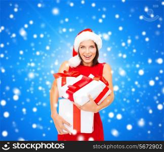 christmas, holidays, celebration and people concept - smiling woman in santa helper hat and red dress with gift boxes over blue snowing background