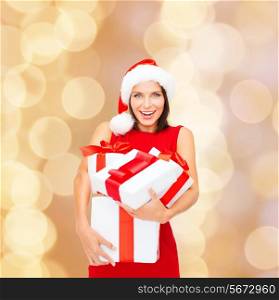 christmas, holidays, celebration and people concept - smiling woman in santa helper hat and red dress with gift boxes over beige lights background