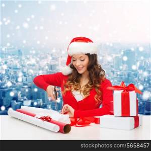 christmas, holidays, celebration, decoration and people concept - smiling woman in santa helper hat with scissors packing gift box over snowy city background