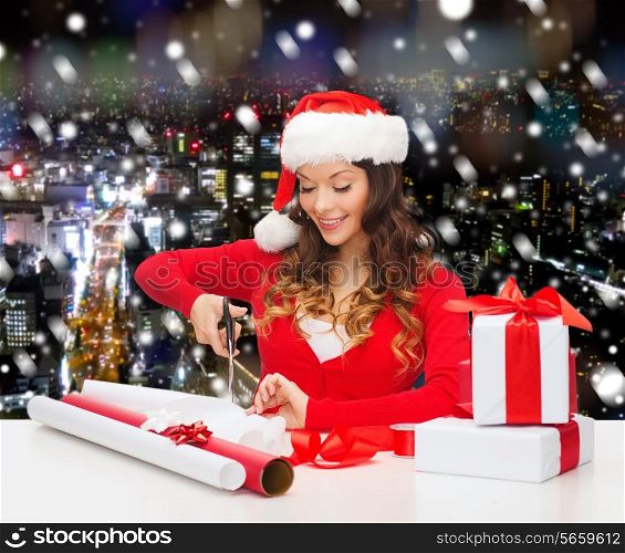 christmas, holidays, celebration, decoration and people concept - smiling woman in santa helper hat with scissors packing gift box over snowy night city background