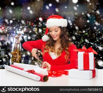 christmas, holidays, celebration, decoration and people concept - smiling woman in santa helper hat with scissors packing gift box over snowy night city background
