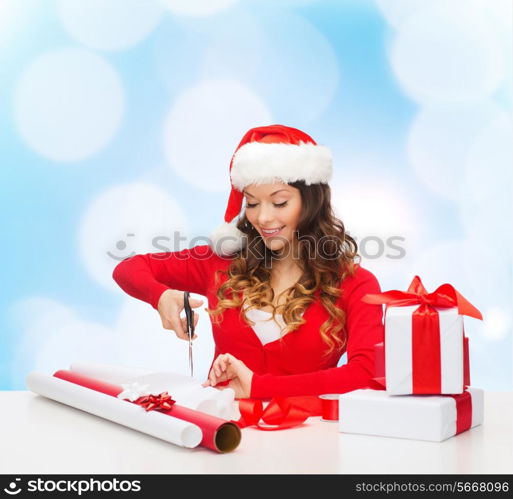 christmas, holidays, celebration, decoration and people concept - smiling woman in santa helper hat with scissors packing gift box over blue lights background