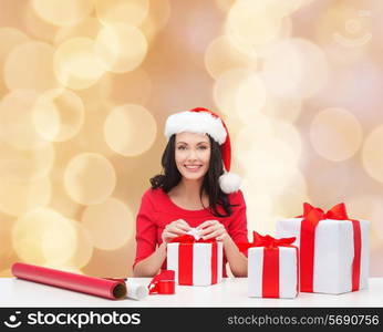 christmas, holidays, celebration, decoration and people concept - smiling woman in santa helper hats with decorating paper and gift boxes over beige lights background