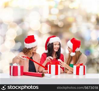 christmas, holidays, celebration, decoration and people concept - smiling women in santa helper hats with decorating paper and gift boxes over lights background