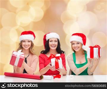 christmas, holidays, celebration, decoration and people concept - smiling women in santa helper hats with decorating paper and gift boxes over beige lights background