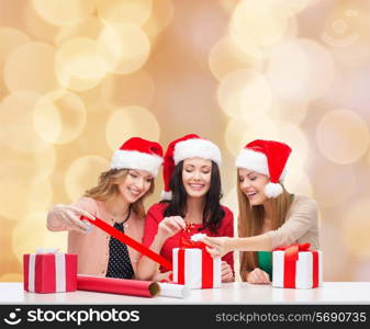 christmas, holidays, celebration, decoration and people concept - smiling women in santa helper hats with decorating paper and gift boxes over beige lights background