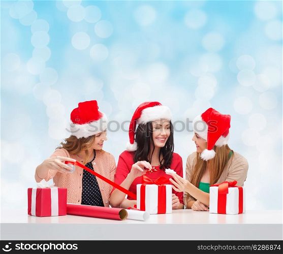 christmas, holidays, celebration, decoration and people concept - smiling women in santa helper hats with decorating paper and gift boxes over blue lights background