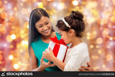 christmas, holidays, celebration, family and people concept - happy mother and child girl with gift box over lights background