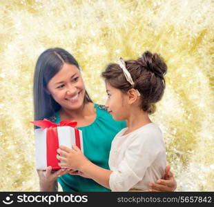 christmas, holidays, celebration, family and people concept - happy mother and child girl with gift box over golden lights background