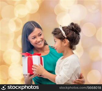 christmas, holidays, celebration, family and people concept - happy mother and child girl with gift box over beige lights background