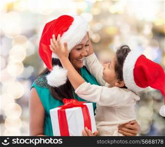 christmas, holidays, celebration, family and people concept - happy mother and child girl in santa helper hats with gift box over lights background