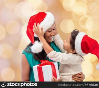 christmas, holidays, celebration, family and people concept - happy mother and child girl in santa helper hats with gift box over beige lights background