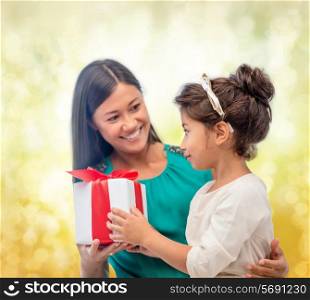 christmas, holidays, celebration, family and people concept - happy mother and child girl with gift box over yellow lights background