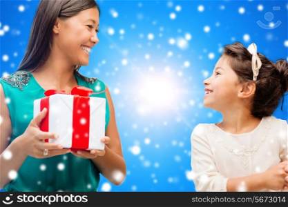 christmas, holidays, celebration, family and people concept - happy mother and girl with gift box over blue snowy background
