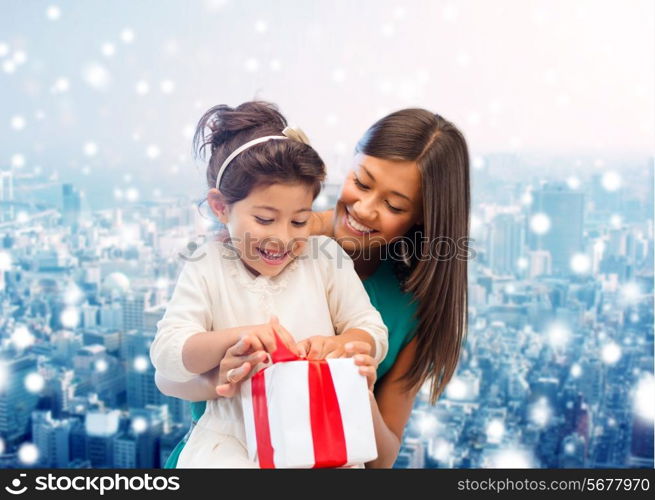 christmas, holidays, celebration, family and people concept - happy mother and girl with gift box over snowy city background