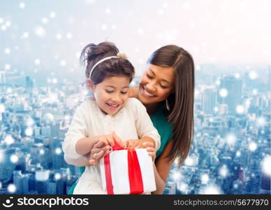 christmas, holidays, celebration, family and people concept - happy mother and girl with gift box over snowy city background