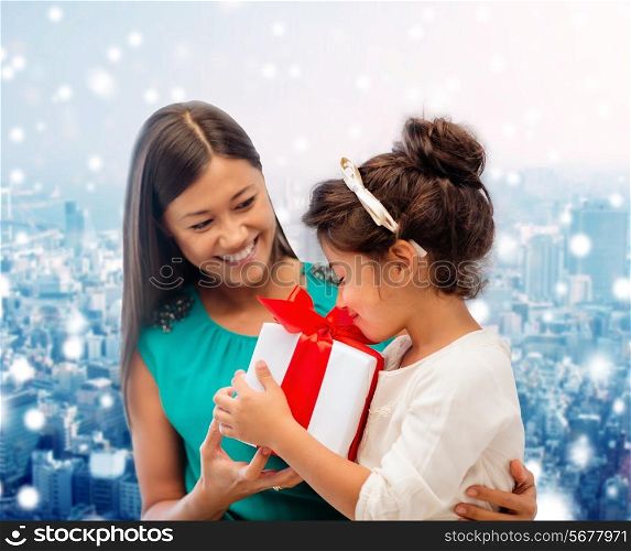 christmas, holidays, celebration, family and people concept - happy mother and girl with gift box over snowy city background