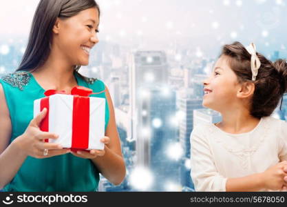 christmas, holidays, celebration, family and people concept - happy mother and girl with gift box over snowy city background