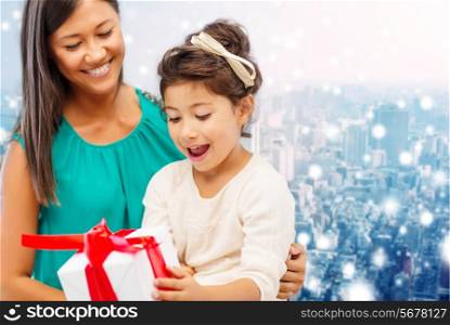 christmas, holidays, celebration, family and people concept - happy mother and girl with gift box over snowy city background