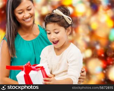christmas, holidays, celebration, family and people concept - happy mother and little girl with gift box over red lights background