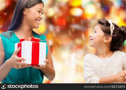 christmas, holidays, celebration, family and people concept - happy mother and little girl with gift box over red lights background
