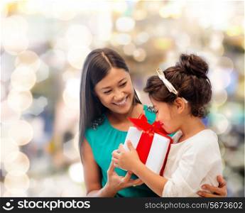 christmas, holidays, celebration, family and people concept - happy mother and little girl with gift box over lights background