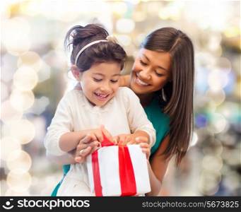 christmas, holidays, celebration, family and people concept - happy mother and little girl with gift box over lights background