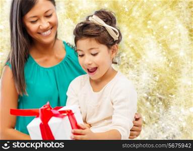 christmas, holidays, celebration, family and people concept - happy mother and little girl with gift box over yellow lights background