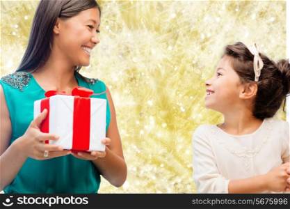 christmas, holidays, celebration, family and people concept - happy mother and little girl with gift box over yellow lights background
