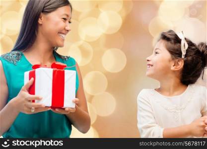 christmas, holidays, celebration, family and people concept - happy mother and little girl with gift box over beige lights background