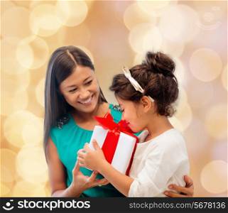 christmas, holidays, celebration, family and people concept - happy mother and little girl with gift box over beige lights background