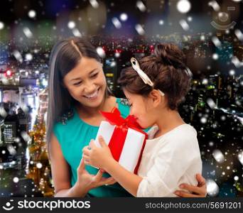 christmas, holidays, celebration, family and people concept - happy mother and little girl with gift box over snowy night city background