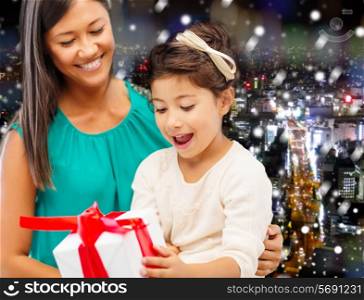 christmas, holidays, celebration, family and people concept - happy mother and little girl with gift box over snowy night city background