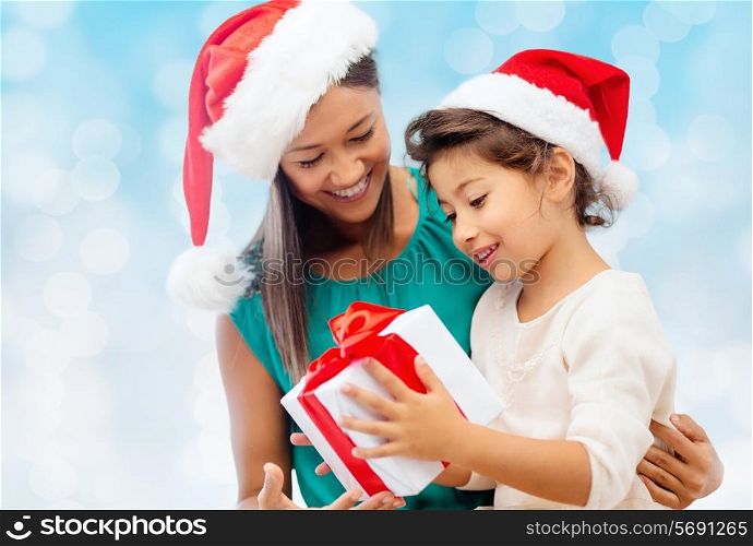 christmas, holidays, celebration, family and people concept - happy mother and little girl in santa helper hats with gift box over blue lights background