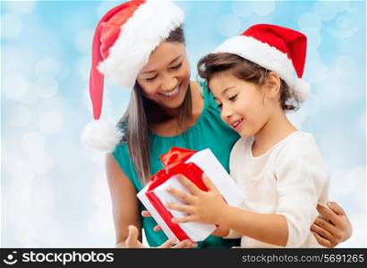 christmas, holidays, celebration, family and people concept - happy mother and little girl in santa helper hats with gift box over blue lights background