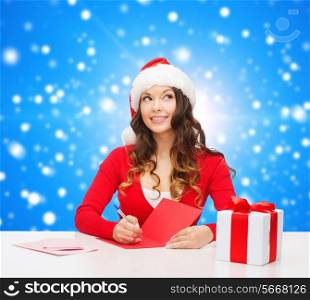 christmas, holidays, celebration, greeting and people concept - smiling woman in santa helper hat with gift box writing letter or sending post card over blue snowy background