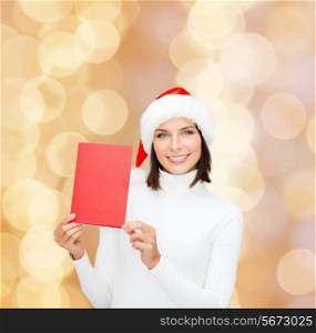 christmas, holidays, celebration, greeting and people concept - smiling woman in santa helper hat with greeting card over beige lights background