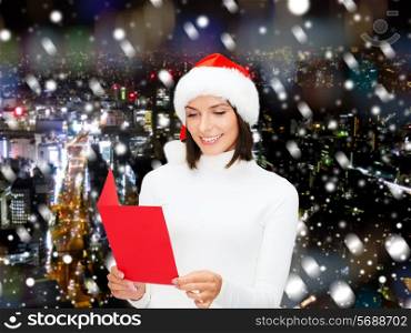 christmas, holidays, celebration, greeting and people concept - smiling woman in santa helper hat with greeting card over snowy night city background