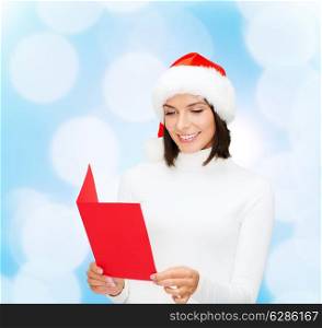 christmas, holidays, celebration, greeting and people concept - smiling woman in santa helper hat with greeting card over blue lights background