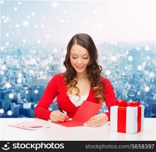 christmas, holidays, celebration, greeting and people concept - smiling woman with gift box writing letter or sending post card over snowy city background