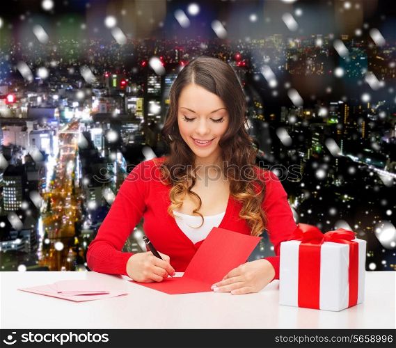christmas, holidays, celebration, greeting and people concept - smiling woman with gift box writing letter or sending post card over snowy night city background