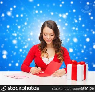 christmas, holidays, celebration, greeting and people concept - smiling woman with gift box writing letter or sending post card over blue snowy background