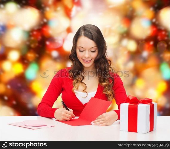 christmas, holidays, celebration, greeting and people concept - smiling woman with gift box writing letter or sending post card over red lights background