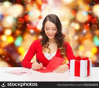 christmas, holidays, celebration, greeting and people concept - smiling woman with gift box writing letter or sending post card over red lights background