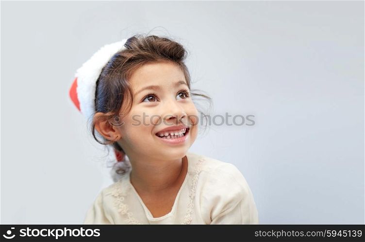 christmas, holidays, childhood and people concept - happy little girl in santa hat over gray background