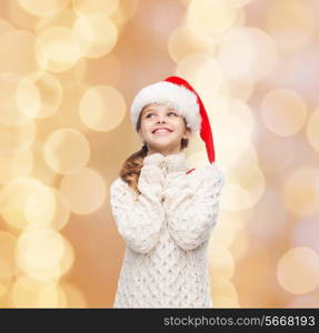 christmas, holidays, childhood and people concept - smiling girl in santa helper hat over beige lights background