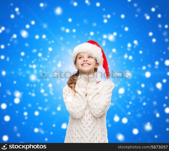 christmas, holidays, childhood and people concept - smiling girl in santa helper hat over blue snowing background