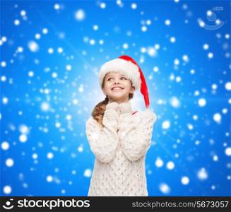 christmas, holidays, childhood and people concept - smiling girl in santa helper hat over blue snowing background